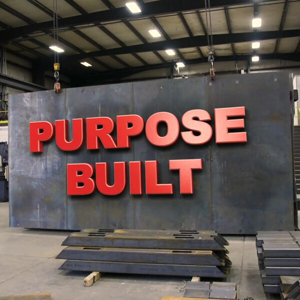 "Purpose Built" text on a large piece of steel hoisted off the ground